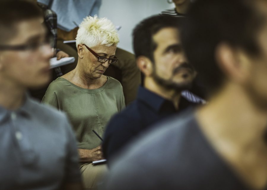 Close up shot of audience in casual clothing listening at seminar, focus on mature woman with glasses in the middle of photography.