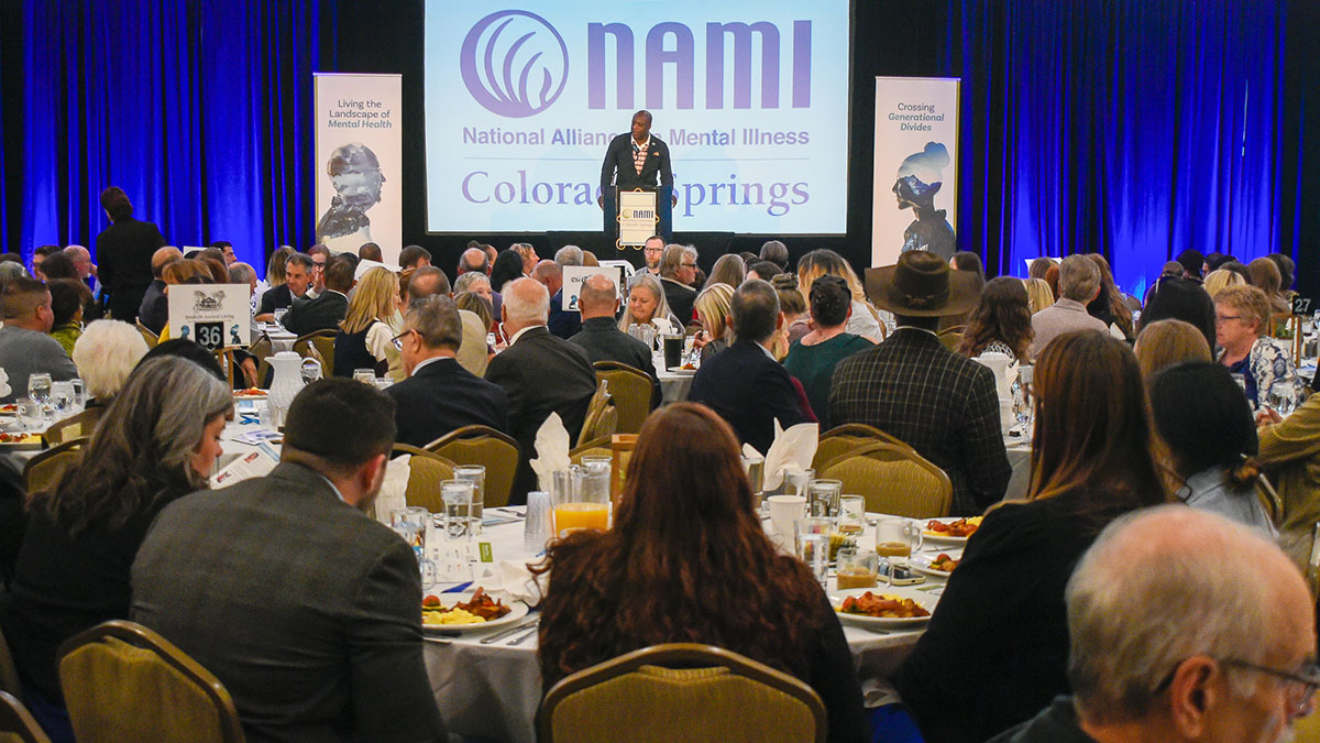 NAMI breakfast speaker at a podium in front of a crowd of attendees seated at tables