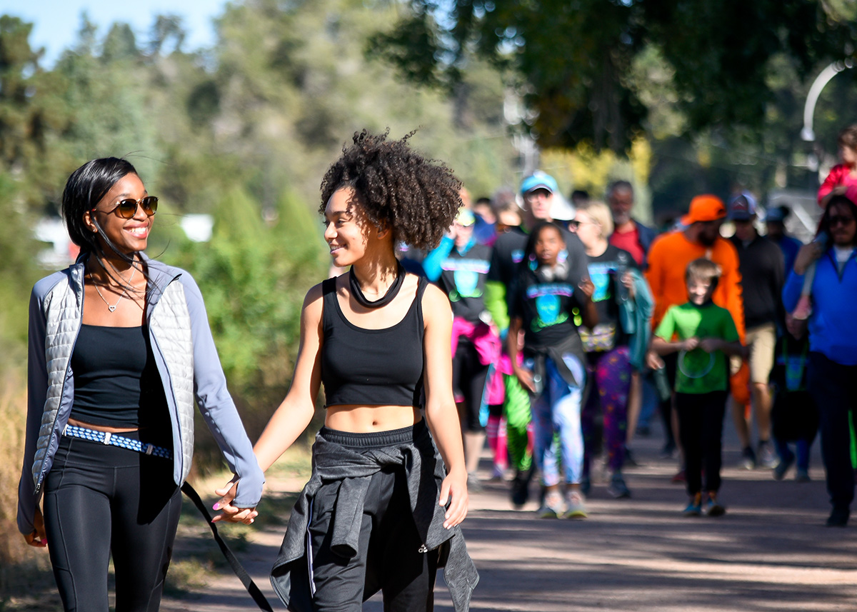 Two people holding hands walking ahead of other people walking in the background