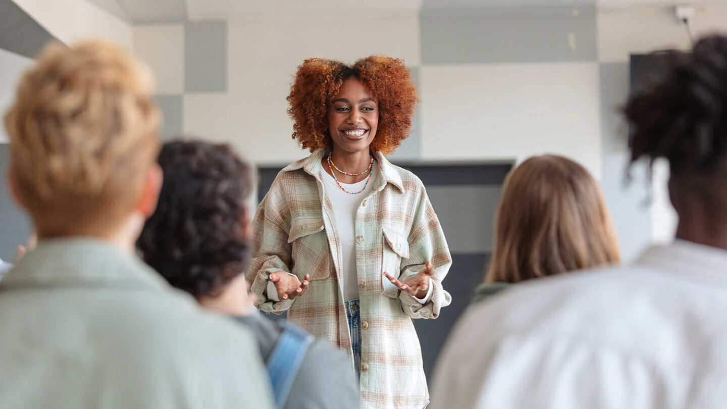 Woman of color speaking to a class of engaged high-school students.