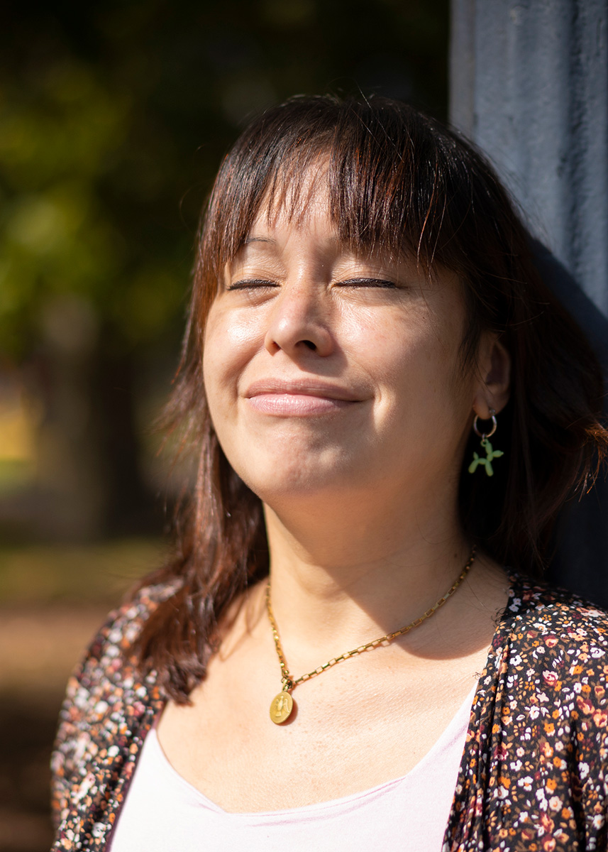 Woman leaning against a pole with her eyes closed feeling sun on her face