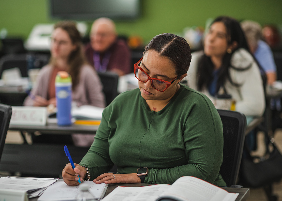 Woman with glasses taking notes in a class for parents